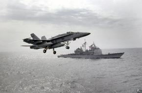 A $94 million F/A-18 Hornet flies past a U.S. warship